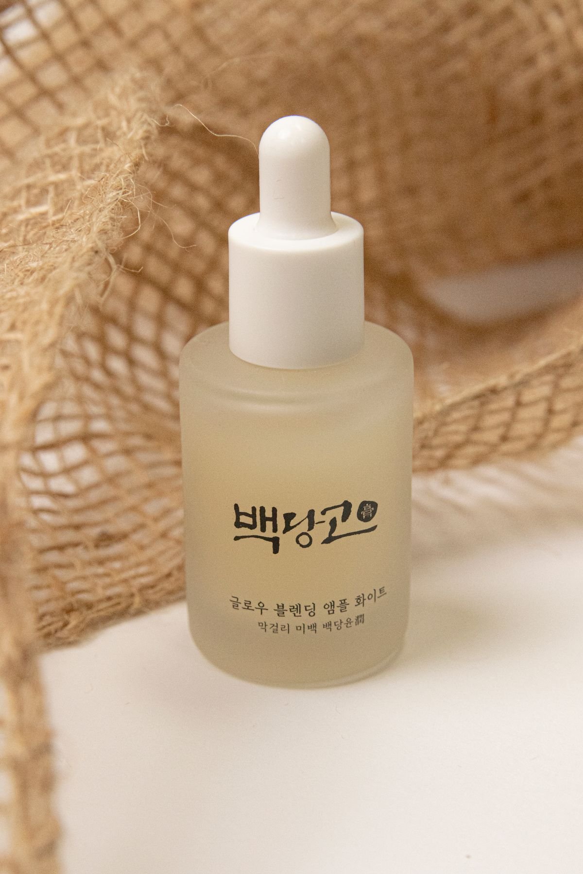 A glass serum bottle on a clean white surface in soft natural light