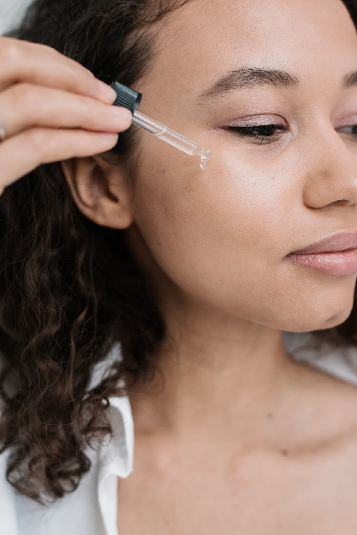 Woman applying skincare serum to her face with a glass dropper during her morning beauty routine