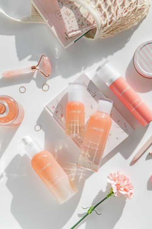 Flat lay of pink-toned Korean skincare bottles and beauty accessories on a soft background