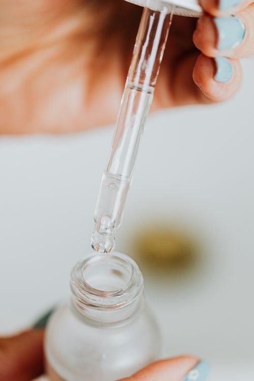 Pipette hovering over a clear serum bottle during a skincare routine